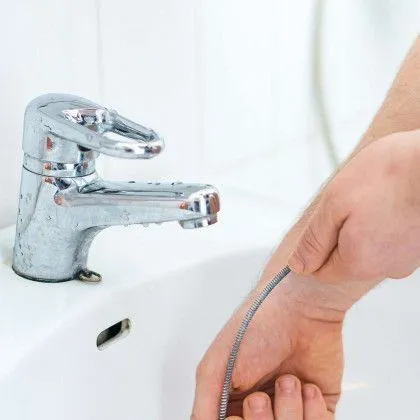 A person is holding a hose in their hand in front of a sink.