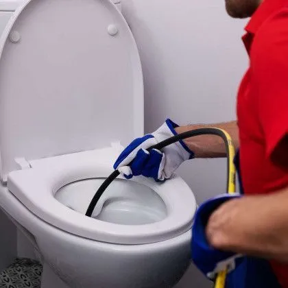 A man is cleaning a toilet with a hose.