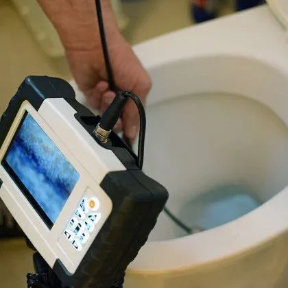 A person is holding a camera in front of a toilet.